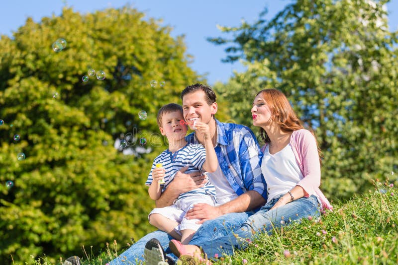 Familia que se sienta en el prado que juega con las burbujas de jabón fotografía de archivo libre de regalías Familia que se sienta en el prado que juega con las burbujas de jabón fotografía de archivo libre de regalías