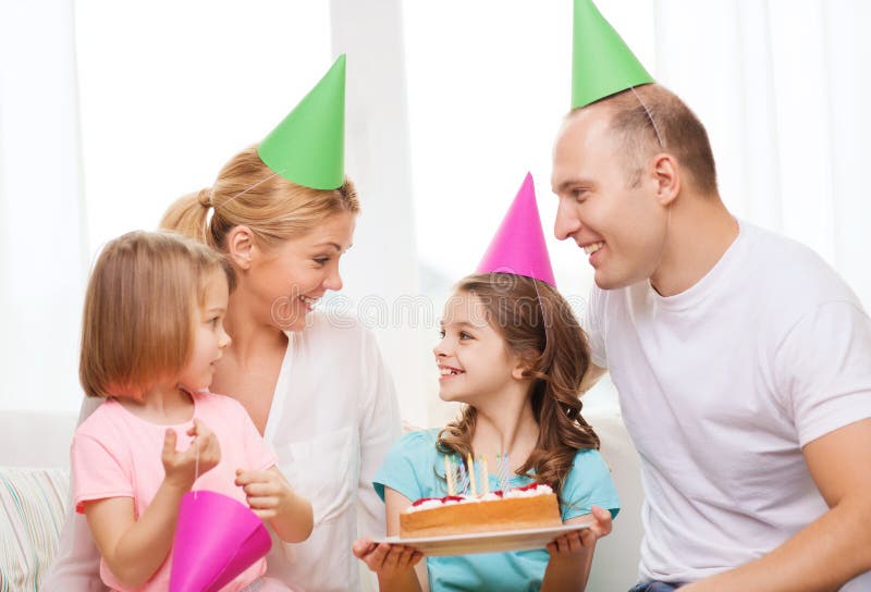 Familia sonriente con dos niños en sombreros con la torta foto de archivo libre de regalías Familia sonriente con dos niños en sombreros con la torta foto de archivo libre de regalías