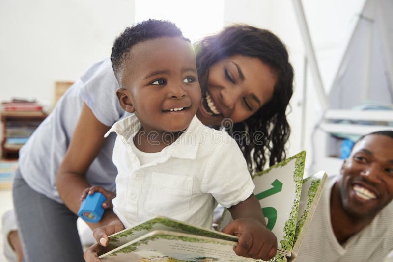 Familie cu copii mici care citesc cărți în sala de joacă împreună stock photography