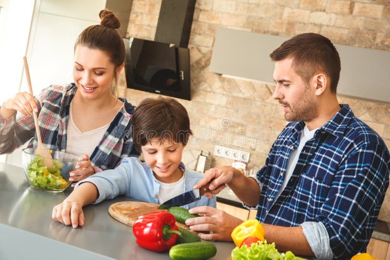 Familie die in keuken zich vader thuis verenigen die zoon scherpe groenten tonen terwijl moeder die gelukkige salade mengen stock foto Familie die in keuken zich vader thuis verenigen die zoon scherpe groenten tonen terwijl moeder die gelukkige salade mengen stock foto