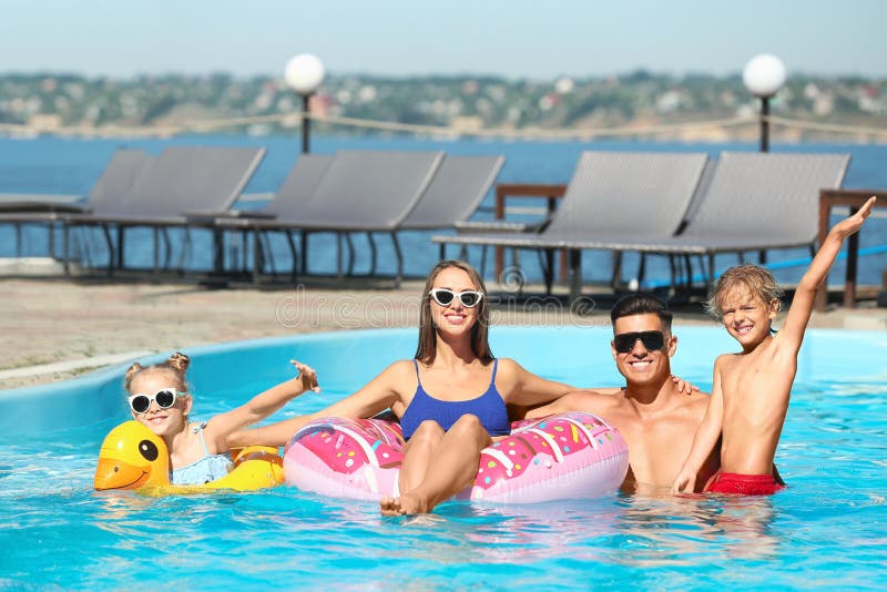 Familie fericită cu inele gonflabile în piscină în aer liber, în ziua însorită de vară stock image