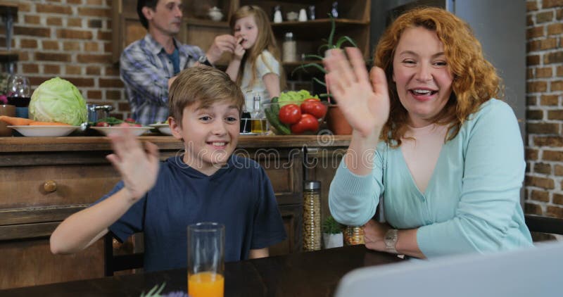 Familie machen Videoanruf unter Verwendung des Laptops beim in den glücklichen Eltern und in den Kindern der Küche bei Tisch siit