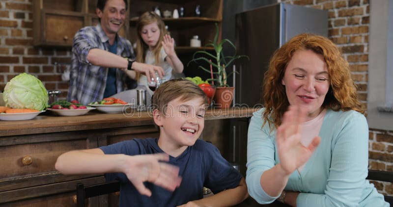 Familie machen Videoanruf unter Verwendung des Laptops beim Kochen des Lebensmittels in den Küchen-glücklichen Eltern und die Kin