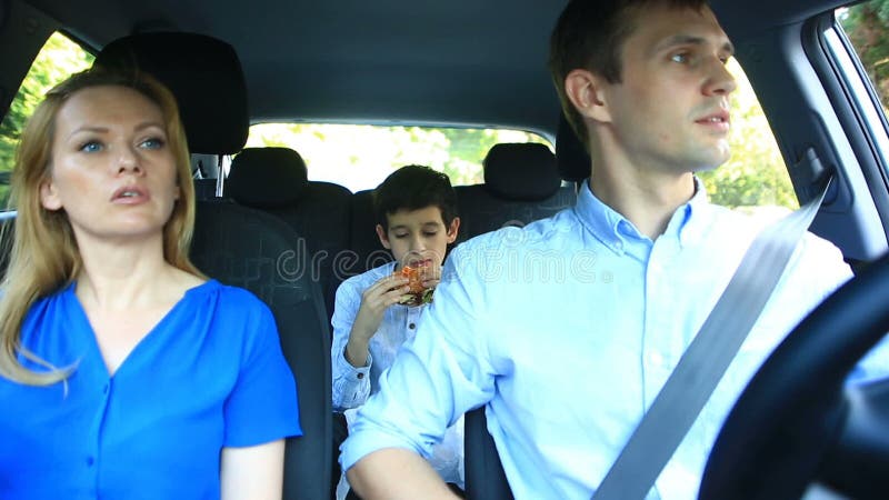 Familie, mammapapa en zoon het berijden in auto, zoon die hamburger eten