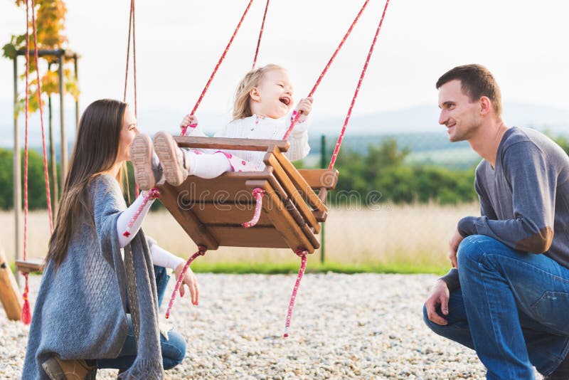Familie met meisje het slingeren op een speelplaats Kinderjaren, Familie, Gelukkig, de Zomer Openluchtconcept royalty-vrije stock foto Familie met meisje het slingeren op een speelplaats Kinderjaren, Familie, Gelukkig, de Zomer Openluchtconcept royalty-vrije stock foto