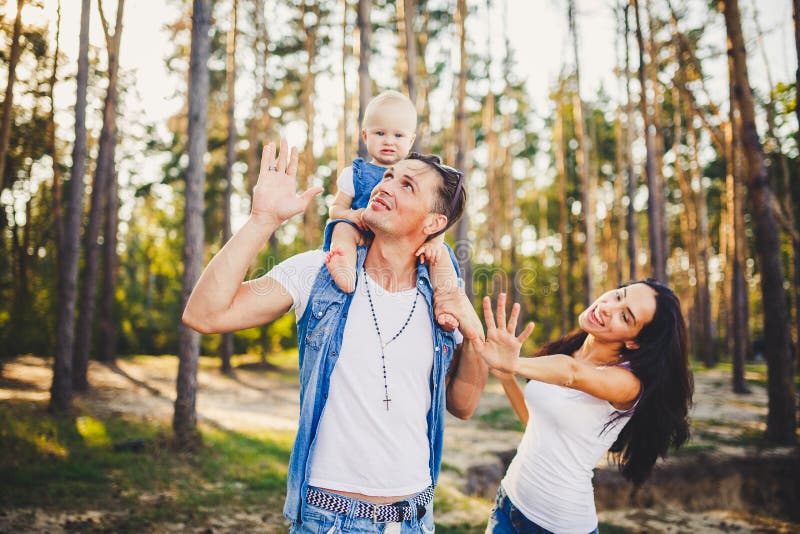 Familienmutter, -vati und -tochter sitzt am Vati auf den Schultern und am Elternkuß auf der Natur im Wald im Sommer an der Sonne lizenzfreies stockfoto Familienmutter, -vati und -tochter sitzt am Vati auf den Schultern und am Elternkuß auf der Natur im Wald im Sommer an der Sonne lizenzfreies stockfoto