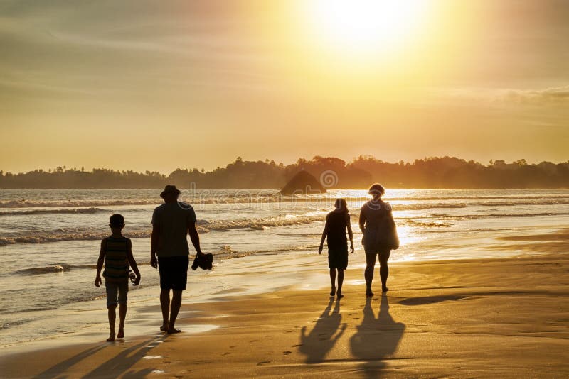 Familievakantie in de keerkringen door het overzees - silhouetten van mensen die op het strand bij zonsondergang lopen stock fotografie Familievakantie in de keerkringen door het overzees - silhouetten van mensen die op het strand bij zonsondergang lopen stock fotografie