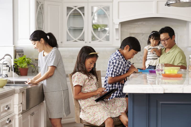 Family In Kitchen Doing Chores And Using Digital Devices. Family In Kitchen Doing Chores And Using Digital Devices