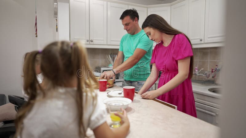 Familj som förbereder frukost tillsammans i ett kozy-kök. Föräldrarna arbetar i disken medan barnen har en juice på arkivfilmer