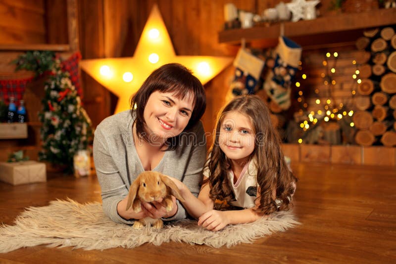 Familjfoto av modern och dottern som lägger på golvet på spisen med gullig kanin julen dekorerar nya home idéer för garnering til arkivfoton Familjfoto av modern och dottern som lägger på golvet på spisen med gullig kanin julen dekorerar nya home idéer för garnering til arkivfoton