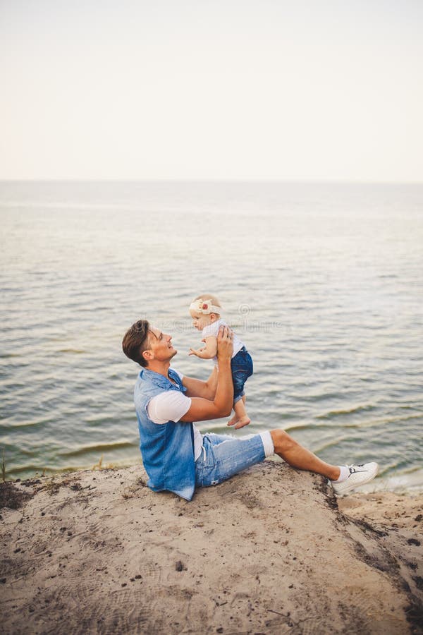Familjsommarsemester i natur fadern och den lilla dottern sitter på den sandiga klippan för ett år med den höga sikten av havet E royaltyfri fotografi Familjsommarsemester i natur fadern och den lilla dottern sitter på den sandiga klippan för ett år med den höga sikten av havet E royaltyfri fotografi