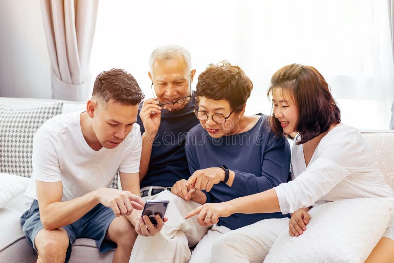 Famille asiatique avec les enfants adultes et les parents supérieurs à l'aide d'un téléphone portable et détendant sur un sofa à photo stock Famille asiatique avec les enfants adultes et les parents supérieurs à l'aide d'un téléphone portable et détendant sur un sofa à photo stock