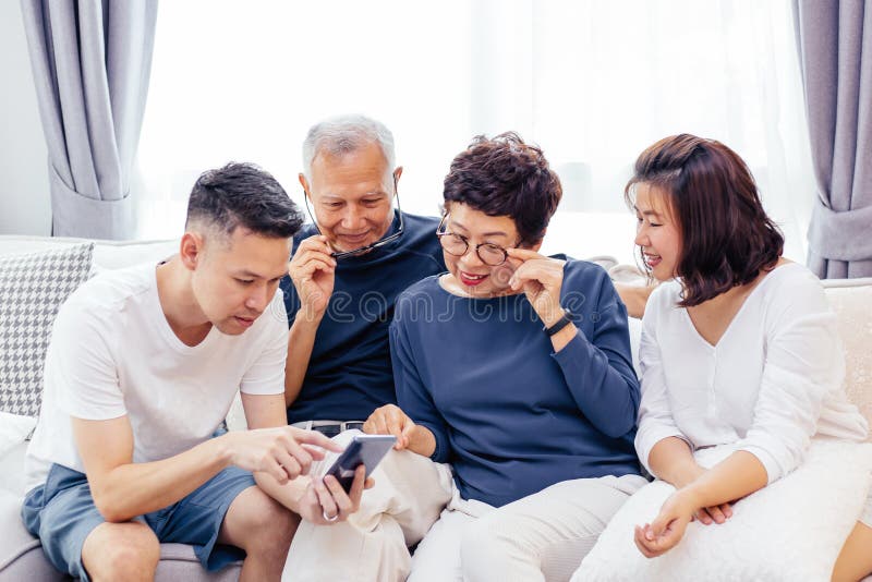 Famille asiatique avec les enfants adultes et les parents supérieurs à l'aide d'un téléphone portable et détendant sur un sofa à images stock Famille asiatique avec les enfants adultes et les parents supérieurs à l'aide d'un téléphone portable et détendant sur un sofa à images stock