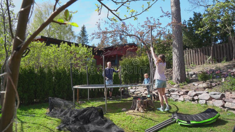 Famille assembler trampoline dans la cour pendant le printemps ensoleillé. banque de vidéos