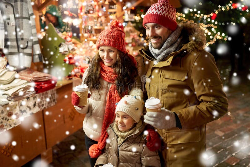 Family, winter holidays and celebration concept - happy mother, father and little daughter with takeaway drinks at christmas market on town hall square in tallinn, estonia over snow. Family, winter holidays and celebration concept - happy mother, father and little daughter with takeaway drinks at christmas market on town hall square in tallinn, estonia over snow