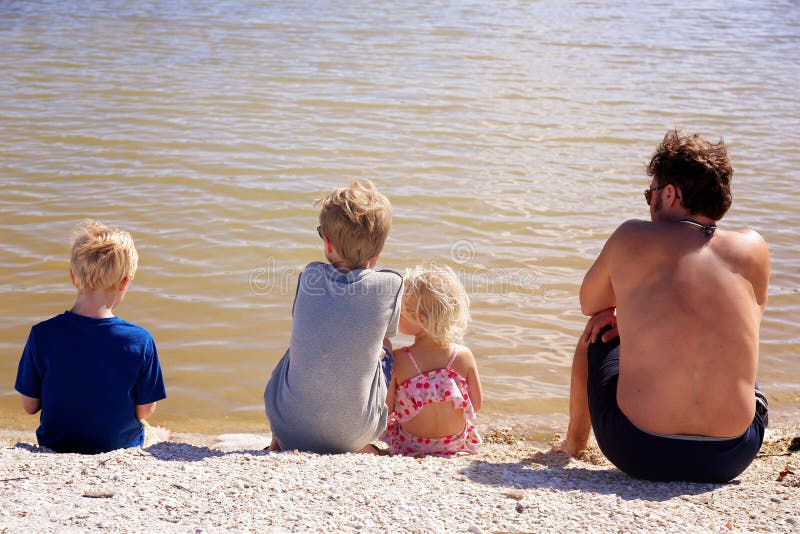 Famille de père et ses enfants s'asseyant sur la plage regardant l'eau photographie stock libre de droits Famille de père et ses enfants s'asseyant sur la plage regardant l'eau photographie stock libre de droits