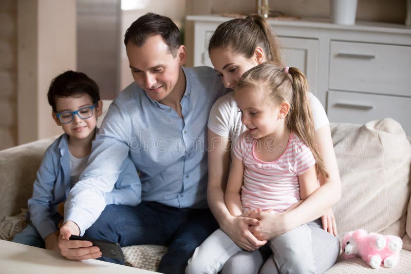 Famille entière observant la vidéo drôle sur le smartphone à la maison images libres de droits Famille entière observant la vidéo drôle sur le smartphone à la maison images libres de droits
