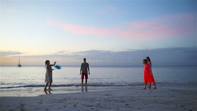 Famille heureuse jouant avec le disque de vol à la plage au coucher du soleil banque de vidéos