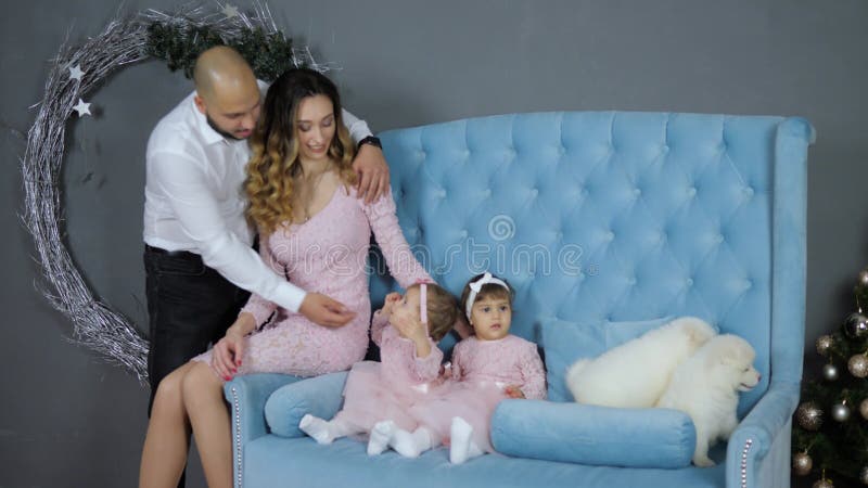 Famille heureuse posant à la séance photo avec deux chiots sur le divan bleu dans le studio