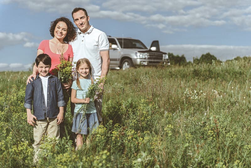 Famille joyeuse se tenant sur le pré près de la voiture photographie stock Famille joyeuse se tenant sur le pré près de la voiture photographie stock