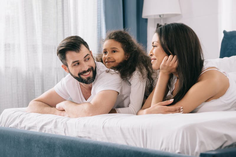 Famille multi-ethnique avec un enfant se situant ensemble dans le lit photos stock Famille multi-ethnique avec un enfant se situant ensemble dans le lit photos stock