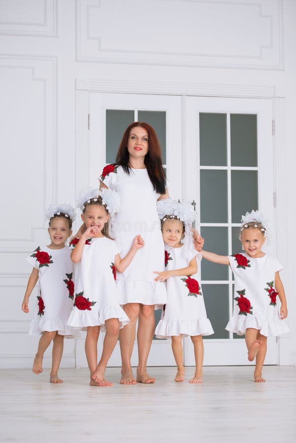 Famille nombreuse heureuse de mère avec quatre filles dans des robes blanches brodées vis-à-vis de la porte dans l'intérieur image stock Famille nombreuse heureuse de mère avec quatre filles dans des robes blanches brodées vis-à-vis de la porte dans l'intérieur image stock