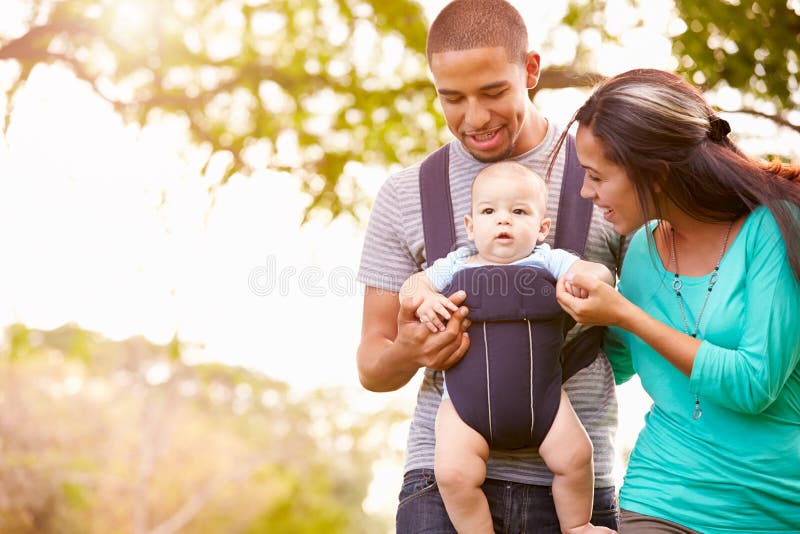 Family With Baby Son In Carrier Walking Through Park