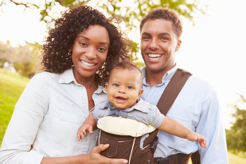 Family With Baby Son In Carrier Walking Through Park