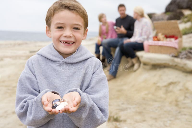 Family at beach with picnic smiling focus on boy with shell. Family at beach with picnic smiling focus on boy with shell