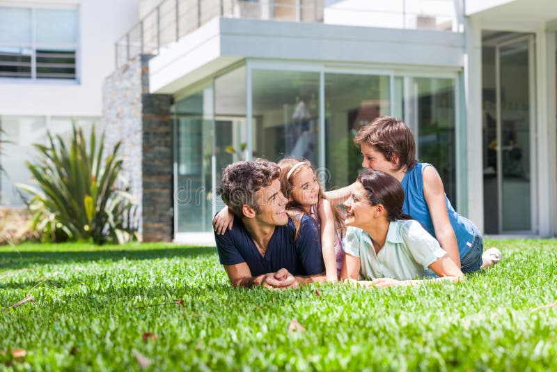 Familia feliz acostada sobre el césped antes casa, padres dos sonrisa.