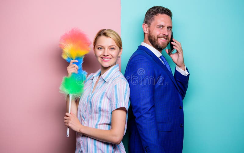 Family couple. Housewife and businessman. Career and housekeeping. Wife stand with dust brush husband has phone royalty free stock photography Family couple. Housewife and businessman. Career and housekeeping. Wife stand with dust brush husband has phone royalty free stock photography