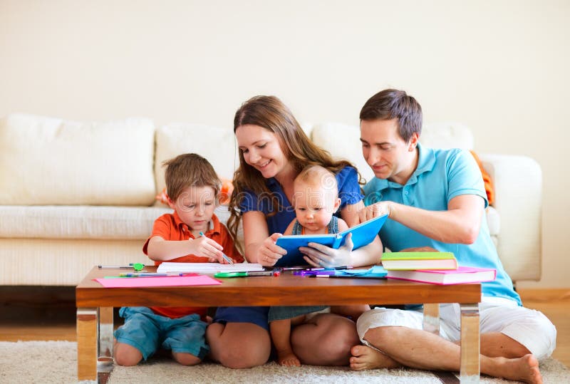 Young happy family with two kids drawing and reading together. Young happy family with two kids drawing and reading together
