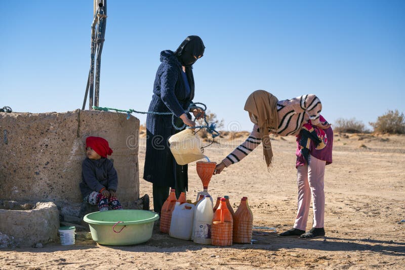 a family drawing water from a well in the desert of Merzouga, Morocco