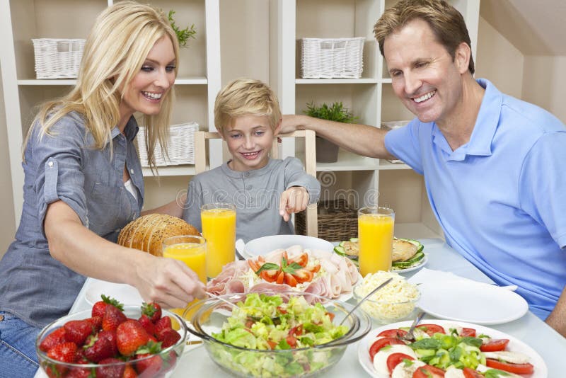 Eine attraktive glücklich, lächelnd Familie mit Mutter, Vater und Sohn Essen Salat und gesundes Essen am Esstisch.