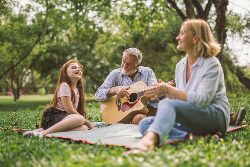 Happy Family Playing Guitar in Their Green Park Garden. Stock Photo