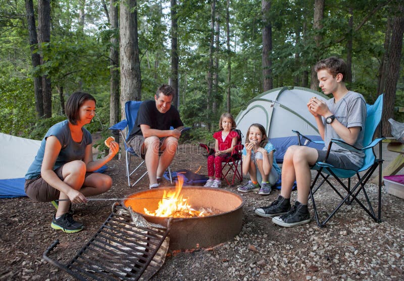 Famiglia di cinque persone per il campeggio e il divertimento di cottura sul fuoco.