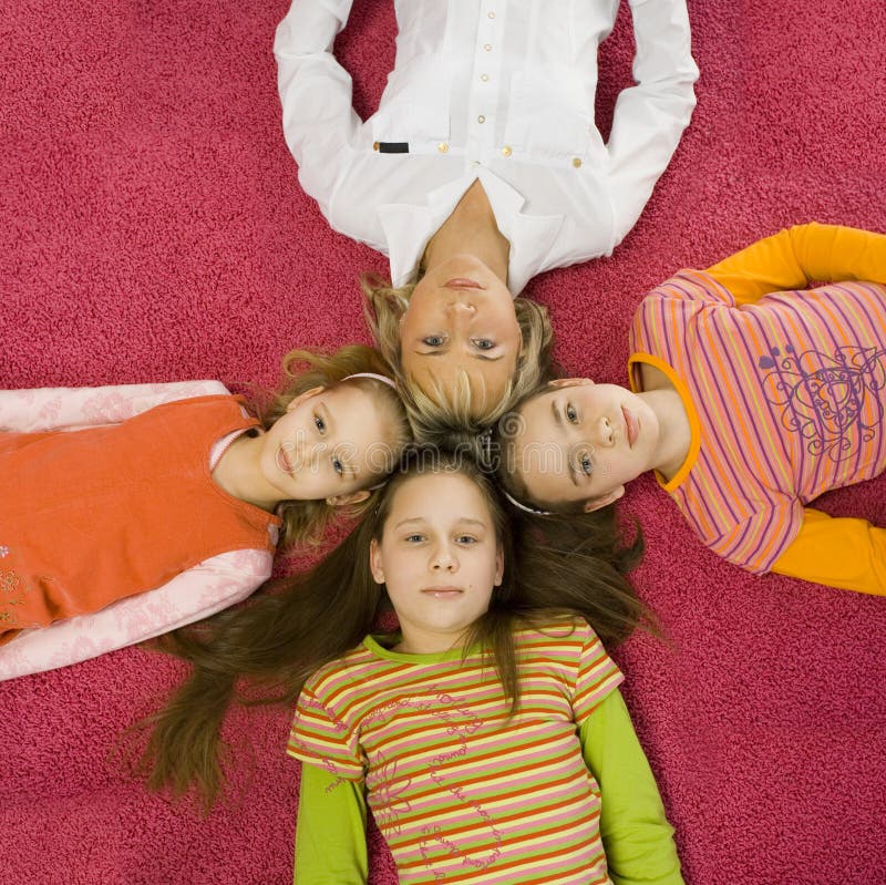 3 girls and their mother are lying on pink carpet and looking at camera. They're touching by their heads. 3 girls and their mother are lying on pink carpet and looking at camera. They're touching by their heads.