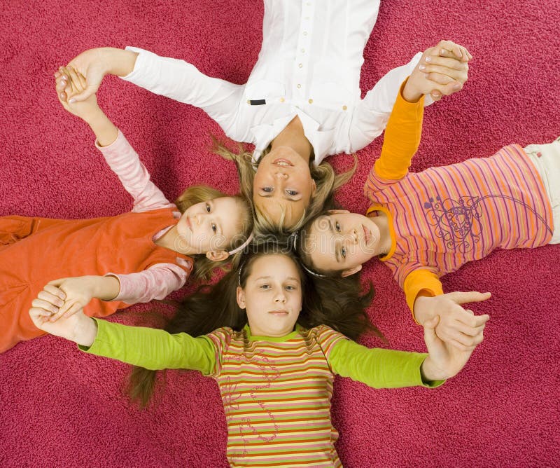 3 girls and their mother are lying on pink carpet and looking at camera. They're touching by their heads. They're holding their hands up. 3 girls and their mother are lying on pink carpet and looking at camera. They're touching by their heads. They're holding their hands up.