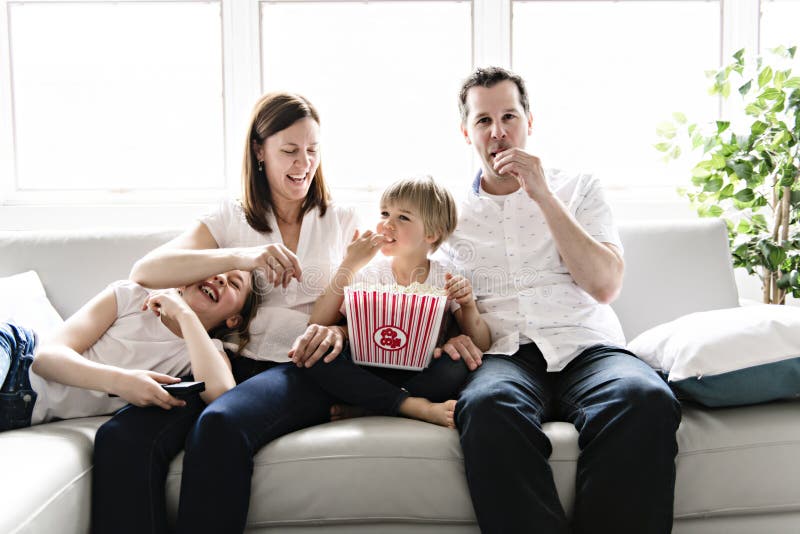 Family of four having fun on the sofa at home watching movie with popcorn