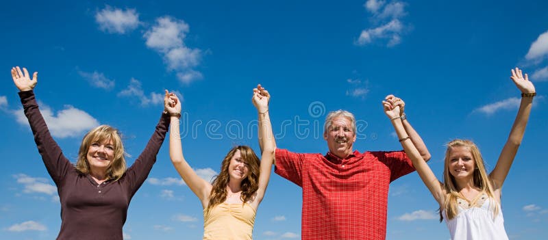 Beautiful family holding hands and raising their arms against a blue sky. Beautiful family holding hands and raising their arms against a blue sky.