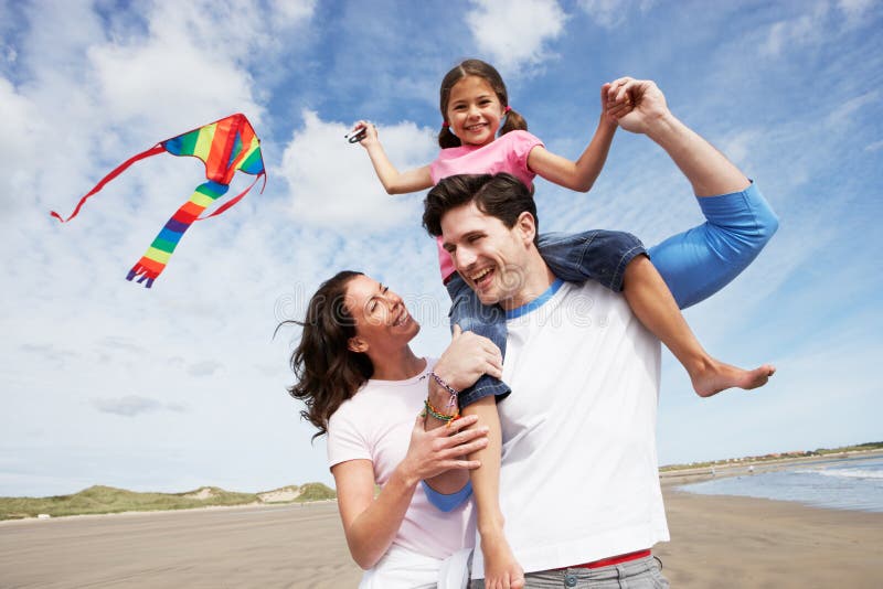 Famiglia Divertimento Di Volo Del Kite Sulla Spiaggia Di Vacanza Sorridente Alla Macchina Fotografica.