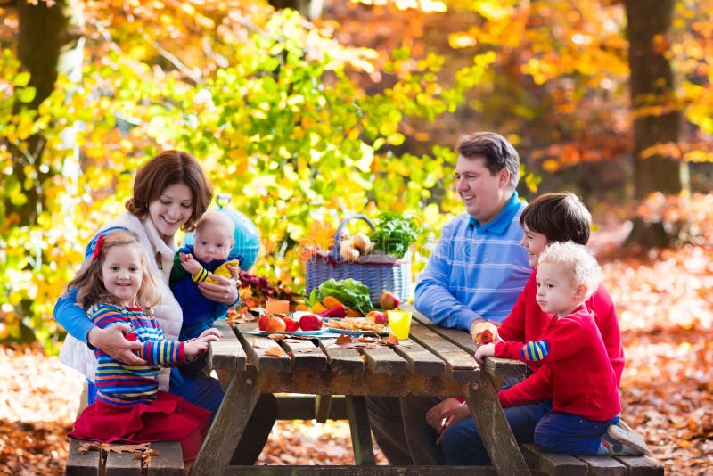 Happy young family with four children grilling meat and making sandwich and salad on a picnic table in sunny autumn park. Barbeque fun for parents with kids on warm fall day. Grill and BBQ party. Happy young family with four children grilling meat and making sandwich and salad on a picnic table in sunny autumn park. Barbeque fun for parents with kids on warm fall day. Grill and BBQ party.