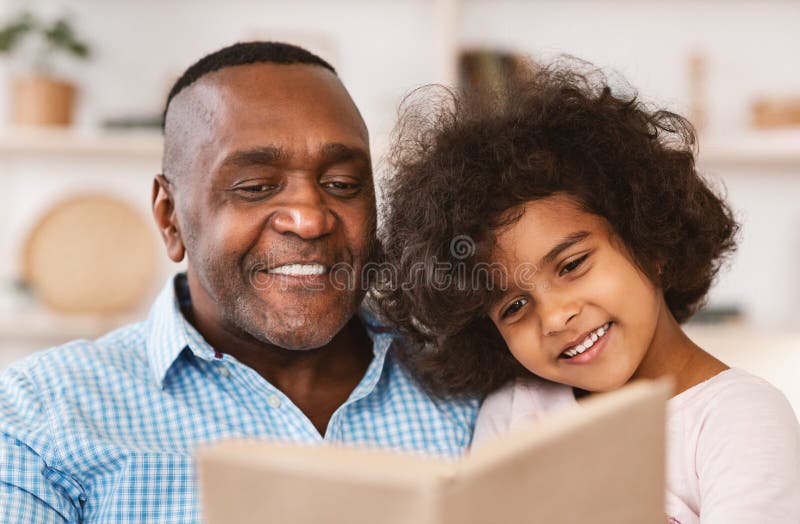 Family lockdown hobbies. African American child listening to her grandfather read bedtime story at home royalty free stock photos