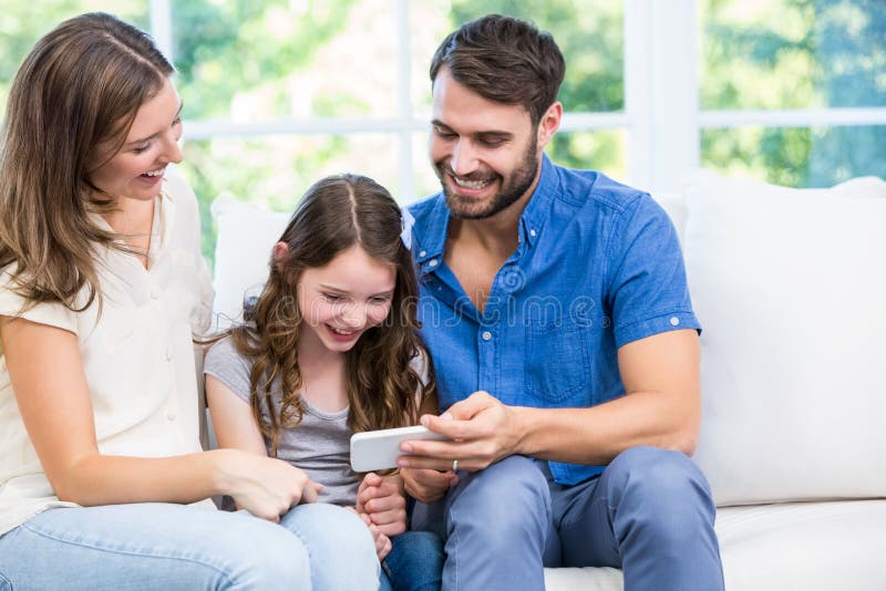 Family looking at smart phone while sitting on sofa royalty free stock photo Family looking at smart phone while sitting on sofa royalty free stock photo