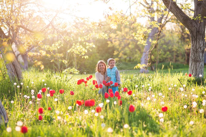 Family mom with daughter woman with child in spring stand and hug on a glade with green grass and tulips