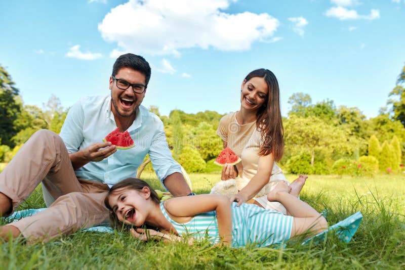 Family In Park. Happy Beautiful Young Parents And Smiling Child Having Fun On Picnic In Park, Kid Eating Fruits. People Relaxing And Spending Time Together Outdoors, In Nature. Relationship Concept. Family In Park. Happy Beautiful Young Parents And Smiling Child Having Fun On Picnic In Park, Kid Eating Fruits. People Relaxing And Spending Time Together Outdoors, In Nature. Relationship Concept