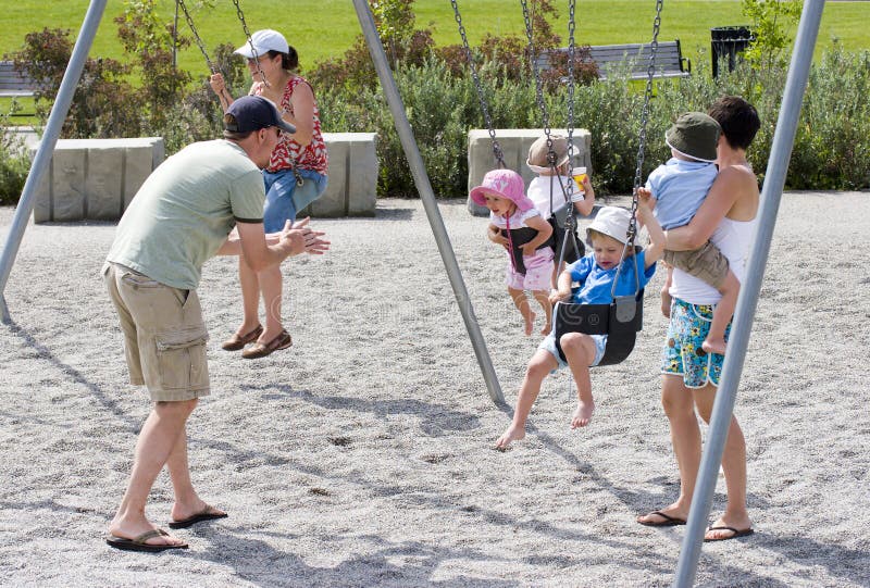 Familia juega sobre el patio de juegos columpios (dos familias) 