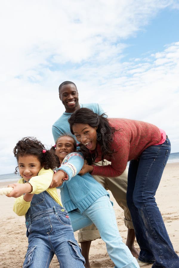 Family playing tug of war on beach having fun