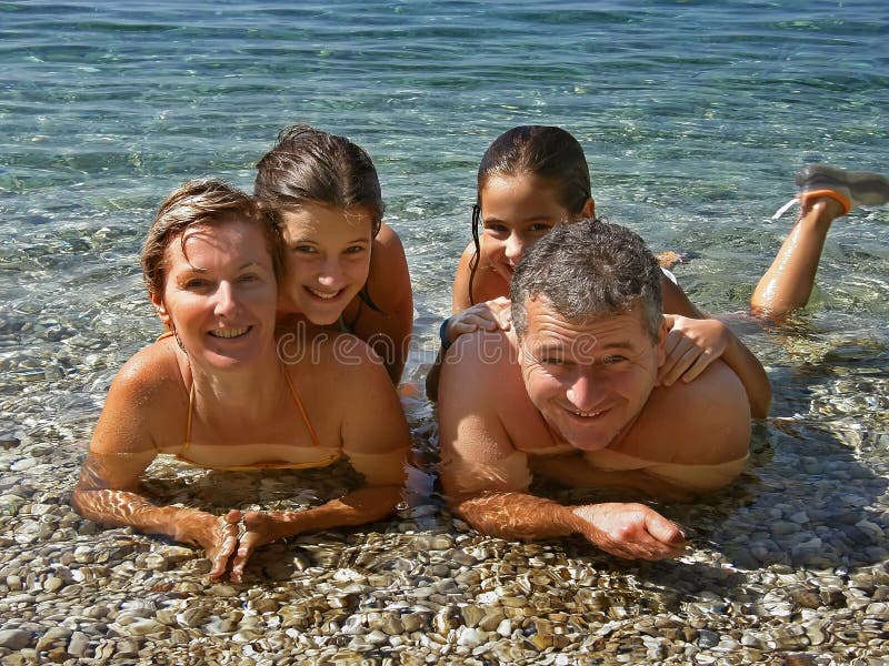 Closeup portrait of happy smiling family (father and mother with two girls - children) lying on the pebbly beach -shallow and enjoy the summer vacation at sunny day in Croatia on the crystal clear Adriatic Sea. Horizontal color photo. Closeup portrait of happy smiling family (father and mother with two girls - children) lying on the pebbly beach -shallow and enjoy the summer vacation at sunny day in Croatia on the crystal clear Adriatic Sea. Horizontal color photo.