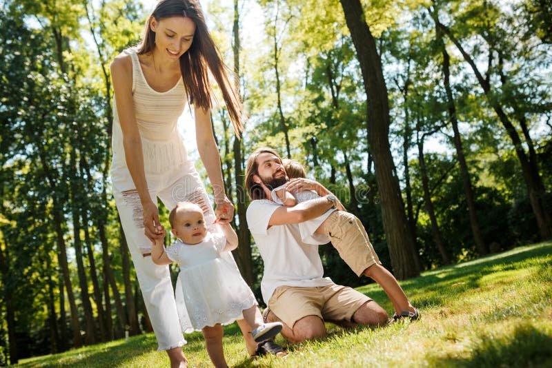 Family rest. Dark-haired mother and father dressed in white clothes are spending summer day with kids on a lawn in the stock photos Family rest. Dark-haired mother and father dressed in white clothes are spending summer day with kids on a lawn in the stock photos